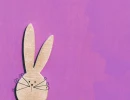 Фиолетовый фон с текстурой краски и деревянной фигуркой кролика с проволочными усами в левой части